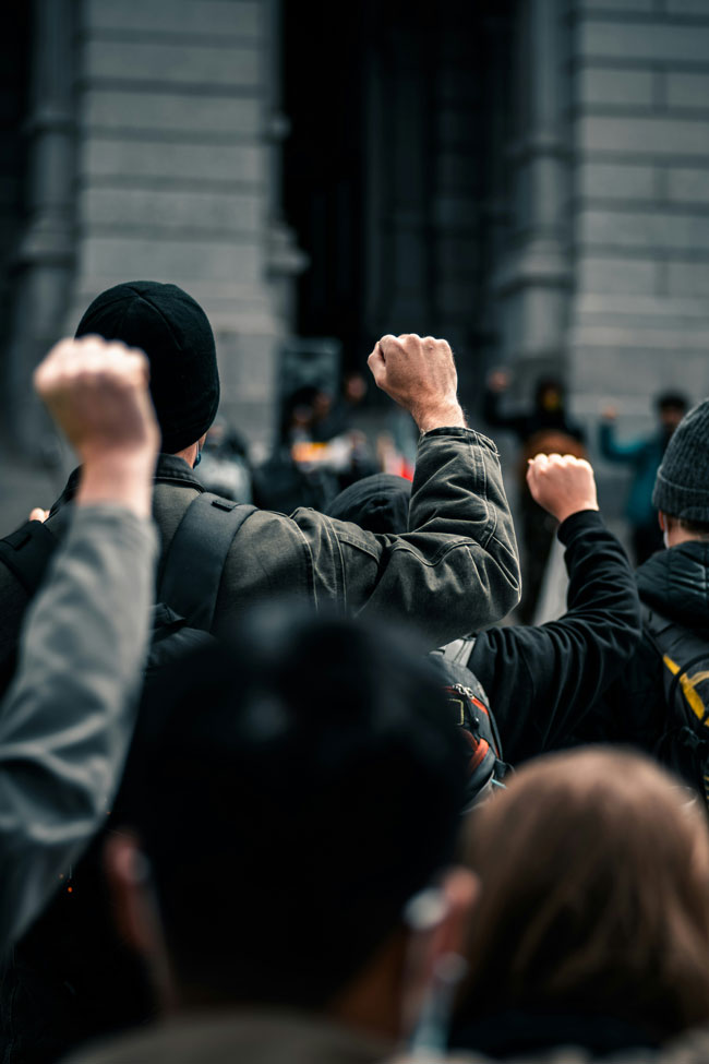 Des hommes qui lèvent le poing lors d'une manifestation - crédit : Colin Lloyd - Unsplash